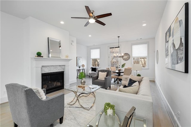 living room featuring a premium fireplace, ceiling fan with notable chandelier, and light hardwood / wood-style flooring