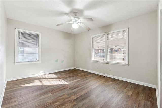 empty room featuring plenty of natural light, dark wood-type flooring, and ceiling fan