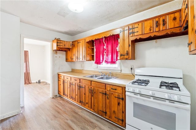 kitchen with white range with gas cooktop, sink, and light wood-type flooring