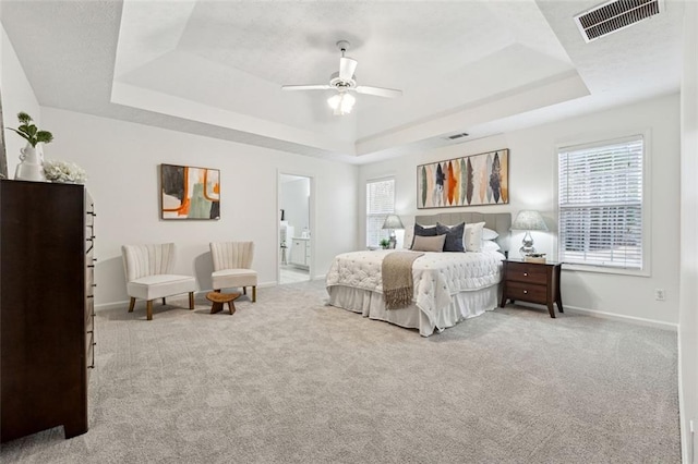 bedroom featuring ceiling fan, ensuite bath, a raised ceiling, and light carpet