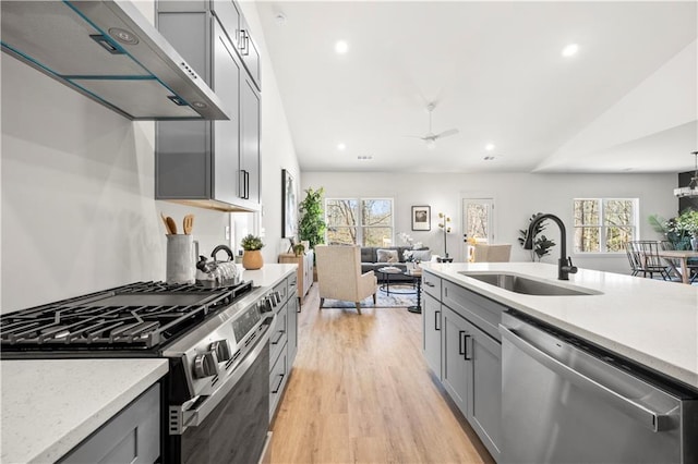 kitchen featuring wall chimney range hood, appliances with stainless steel finishes, gray cabinets, and sink