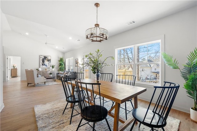 dining space with ceiling fan with notable chandelier, lofted ceiling, and light wood-type flooring