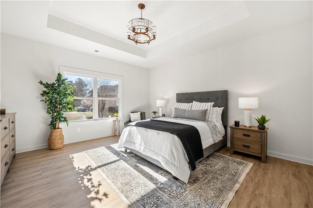 bedroom featuring a raised ceiling, light hardwood / wood-style floors, and an inviting chandelier