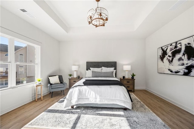 bedroom featuring hardwood / wood-style flooring, a notable chandelier, multiple windows, and a tray ceiling