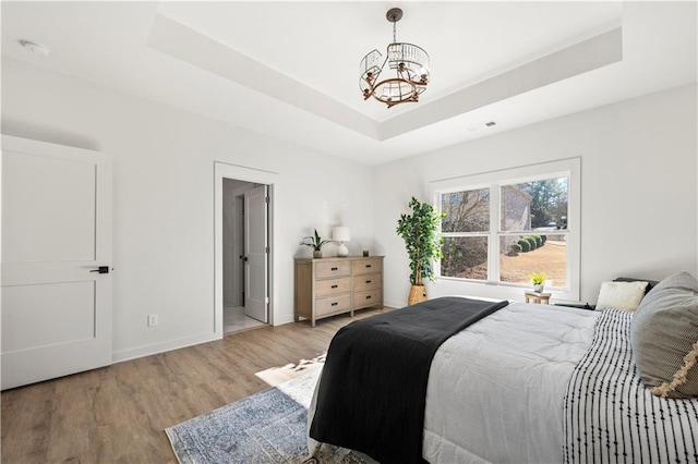 bedroom featuring a tray ceiling, light hardwood / wood-style flooring, and a chandelier