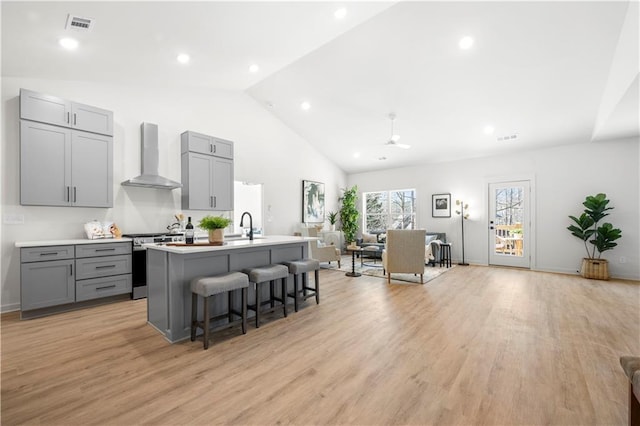 kitchen featuring gray cabinetry, stainless steel range, wall chimney range hood, light hardwood / wood-style flooring, and a center island with sink