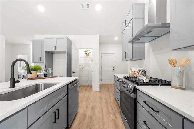 kitchen with sink, wall chimney exhaust hood, stainless steel appliances, light hardwood / wood-style floors, and gray cabinets