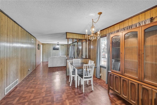 dining space featuring an inviting chandelier, visible vents, wood walls, and a textured ceiling