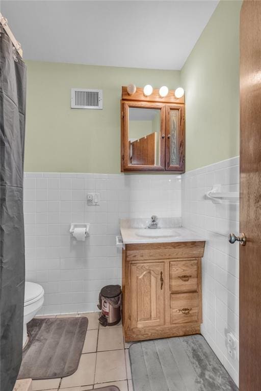 bathroom with visible vents, toilet, tile walls, wainscoting, and vanity