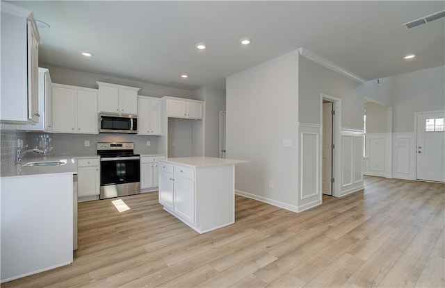 kitchen with appliances with stainless steel finishes, light wood-type flooring, sink, white cabinets, and a kitchen island