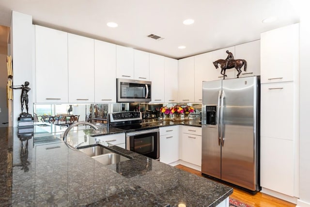 kitchen featuring light wood-type flooring, stainless steel appliances, sink, dark stone countertops, and white cabinets