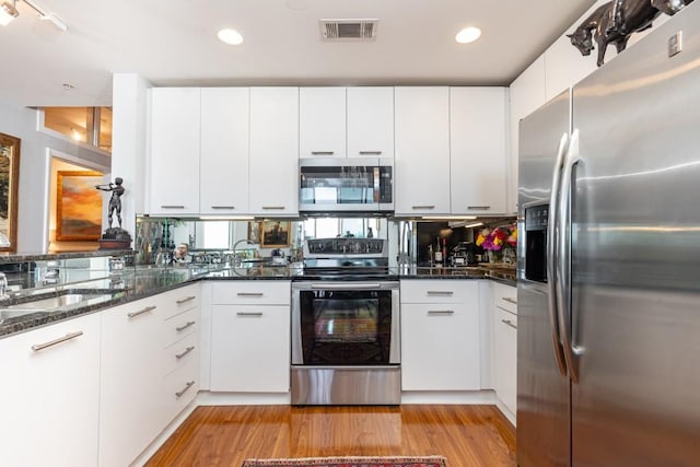 kitchen featuring white cabinets, appliances with stainless steel finishes, light wood-type flooring, and dark stone countertops