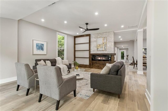 living room with a stone fireplace, light wood-type flooring, and ceiling fan