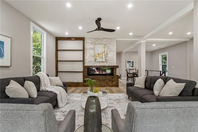 living room featuring a stone fireplace, light wood-type flooring, and ceiling fan