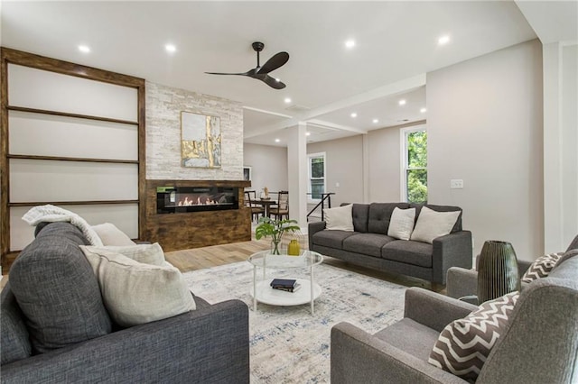 living room featuring a stone fireplace, wood-type flooring, and ceiling fan