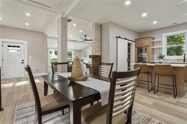 dining area with light hardwood / wood-style floors, a barn door, a wealth of natural light, and ceiling fan