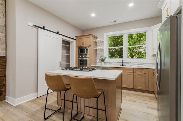 kitchen featuring stainless steel appliances, a barn door, a kitchen island, light hardwood / wood-style floors, and backsplash