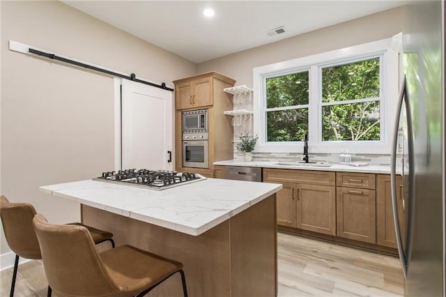 kitchen with a kitchen island, a barn door, light hardwood / wood-style floors, appliances with stainless steel finishes, and sink