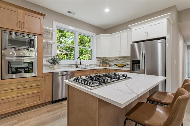 kitchen featuring tasteful backsplash, stainless steel appliances, light wood-type flooring, a center island, and white cabinetry