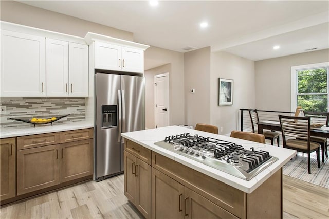 kitchen featuring appliances with stainless steel finishes, light wood-type flooring, tasteful backsplash, and white cabinets