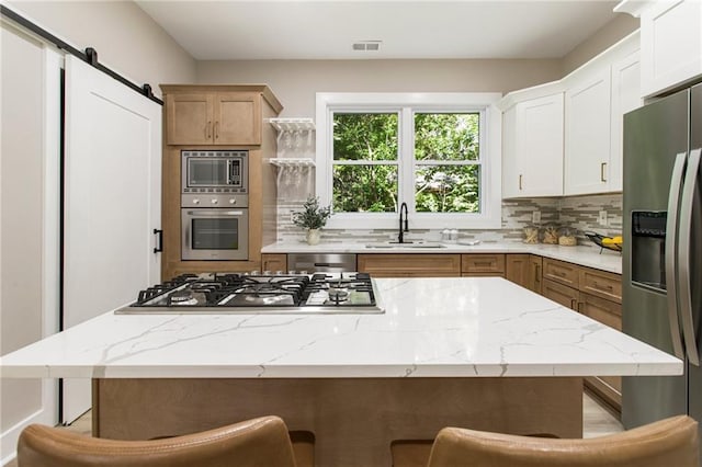 kitchen with tasteful backsplash, white cabinets, a barn door, a center island, and appliances with stainless steel finishes