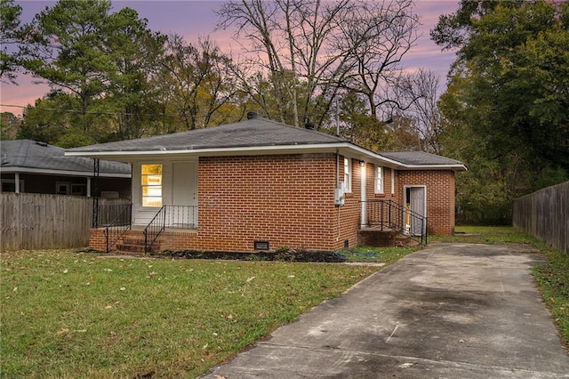 view of front facade with crawl space, a lawn, brick siding, and fence