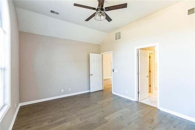 unfurnished bedroom featuring hardwood / wood-style floors, ensuite bath, and vaulted ceiling