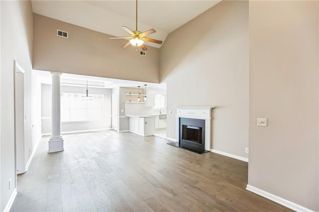 unfurnished living room featuring ornate columns, high vaulted ceiling, hardwood / wood-style flooring, and ceiling fan