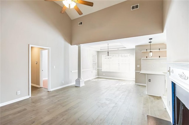 unfurnished living room with ceiling fan, high vaulted ceiling, light wood-type flooring, and ornate columns