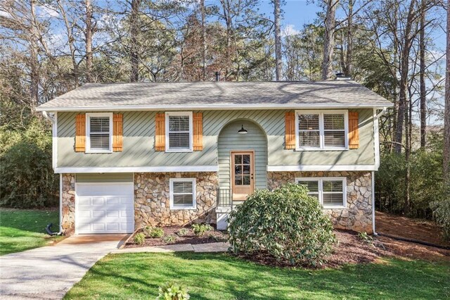 bi-level home with driveway, a front lawn, an attached garage, and stone siding