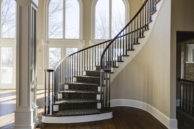 staircase featuring hardwood / wood-style flooring, decorative columns, and a towering ceiling