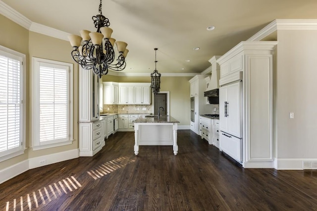 kitchen featuring paneled refrigerator, white cabinetry, a breakfast bar area, and a center island with sink