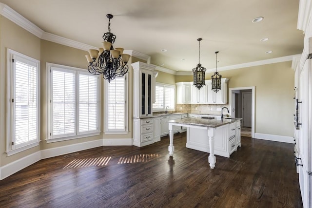 kitchen featuring sink, a breakfast bar, stone counters, ornamental molding, and a center island with sink