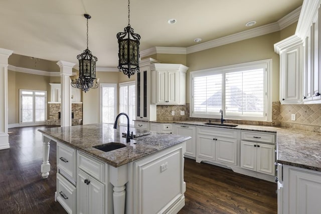 kitchen with white cabinets, sink, an island with sink, and ornate columns