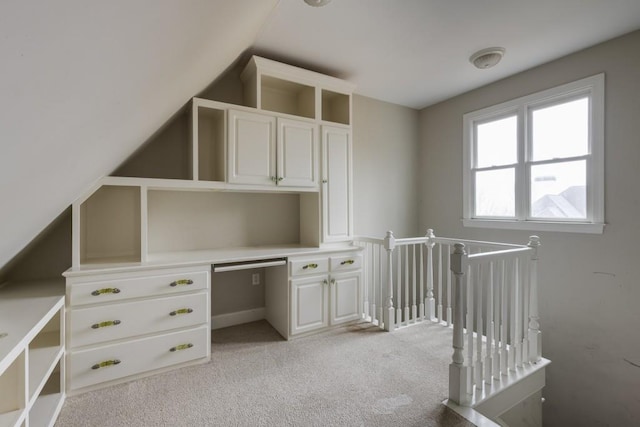 unfurnished office with lofted ceiling, built in desk, and light carpet