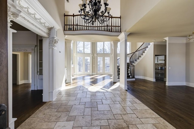 foyer featuring decorative columns, an inviting chandelier, crown molding, a towering ceiling, and light hardwood / wood-style floors