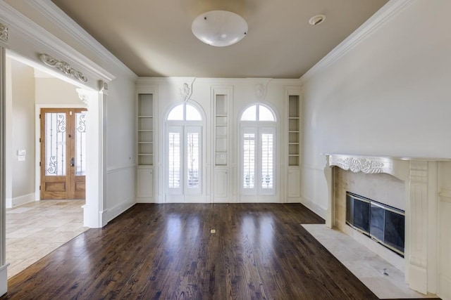 unfurnished living room featuring hardwood / wood-style flooring, ornamental molding, a high end fireplace, and built in features