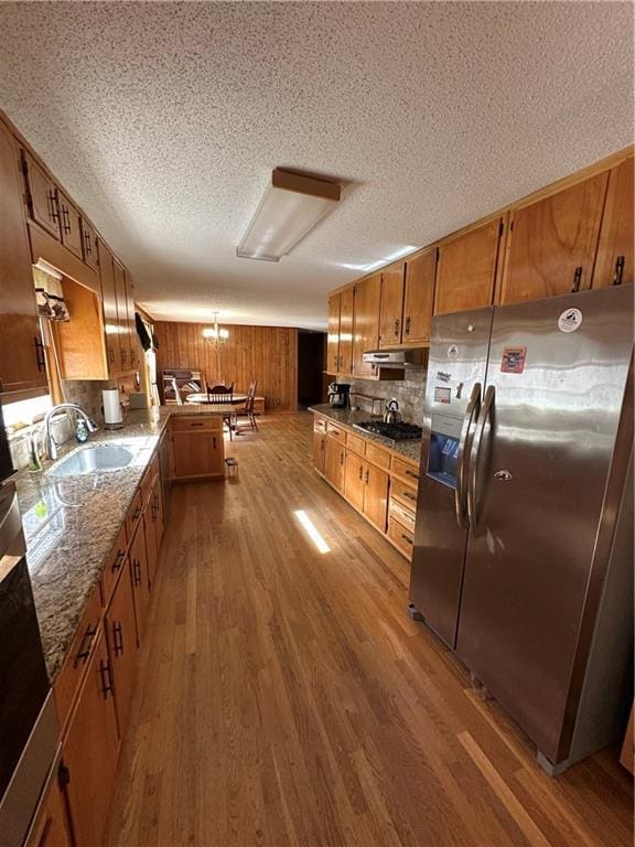 kitchen featuring stainless steel refrigerator with ice dispenser, sink, stone countertops, light wood-type flooring, and gas cooktop