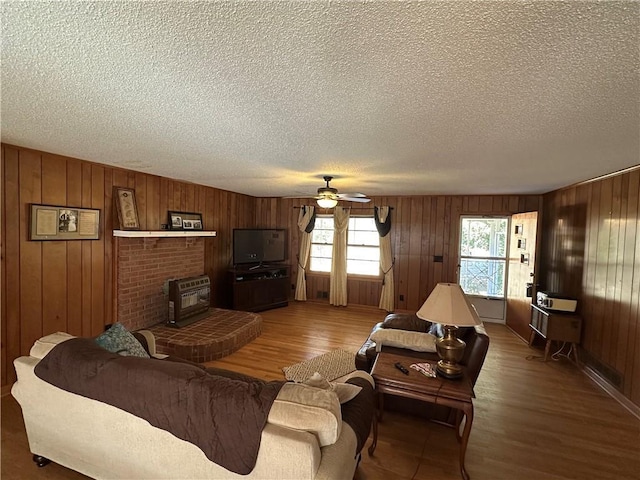 living room with ceiling fan, wood-type flooring, wooden walls, and a textured ceiling