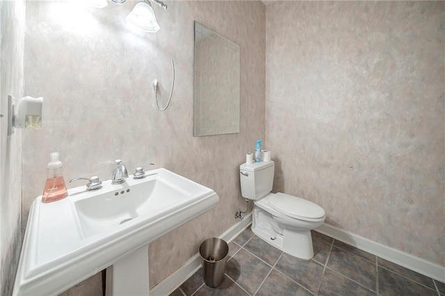 bathroom featuring toilet, a sink, wallpapered walls, tile patterned floors, and baseboards