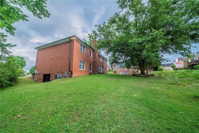 exterior space featuring a yard, a chimney, brick siding, and central AC unit