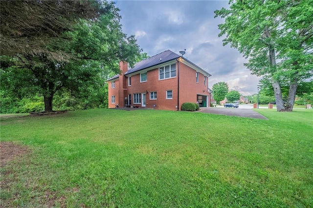 back of house featuring a chimney, driveway, a yard, brick siding, and a garage