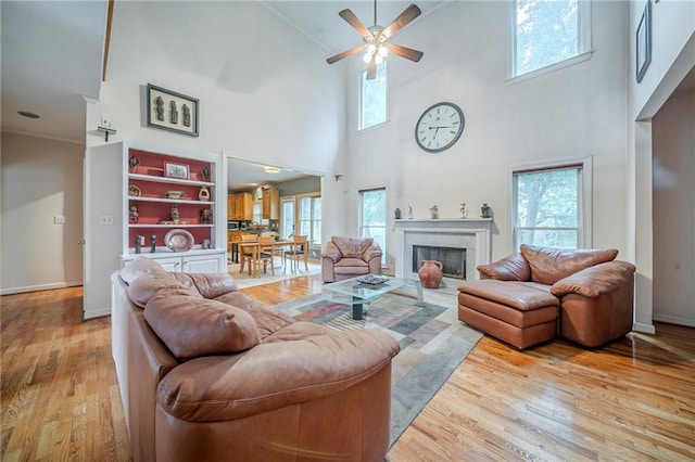living area with ornamental molding, ceiling fan, a high end fireplace, high vaulted ceiling, and wood finished floors
