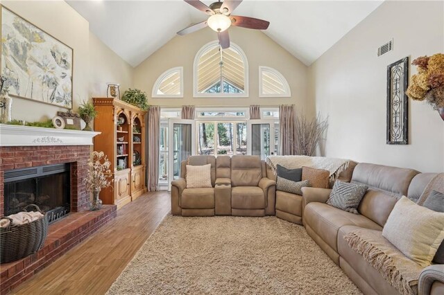 living room with ceiling fan, high vaulted ceiling, a brick fireplace, and light wood-type flooring