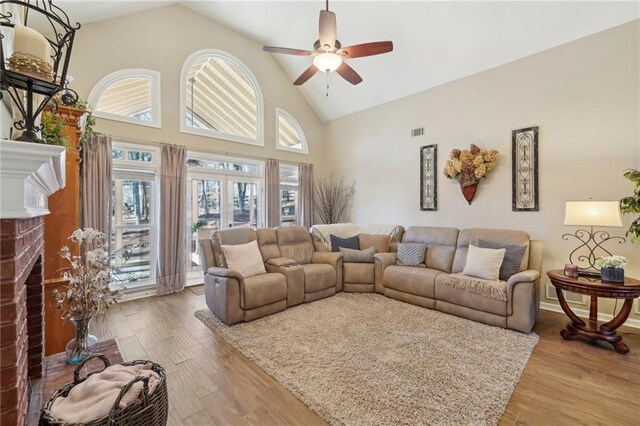 living room with ceiling fan, a fireplace, high vaulted ceiling, and light wood-type flooring