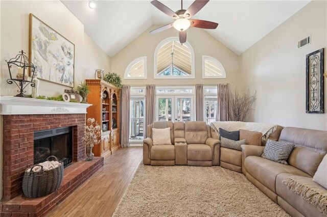 living room with french doors, high vaulted ceiling, hardwood / wood-style flooring, ceiling fan, and a fireplace