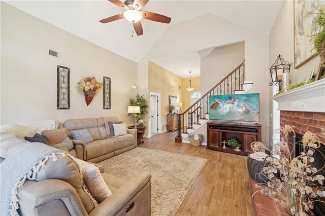 living room featuring ceiling fan, a fireplace, high vaulted ceiling, and light hardwood / wood-style flooring