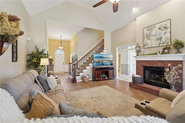 living room with ceiling fan, high vaulted ceiling, a brick fireplace, and light wood-type flooring