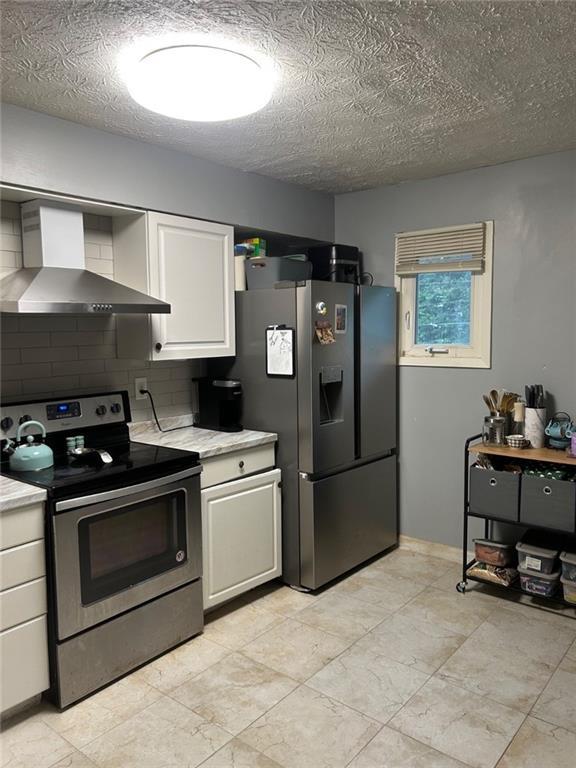 6658 Ramsgate Way, Norcross, GA 30093 - kitchen featuring stainless steel appliances, wall chimney range hood, light countertops, white cabinetry, and a textured ceiling