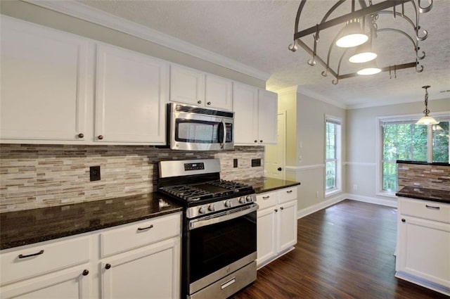 kitchen featuring dark stone countertops, white cabinets, hanging light fixtures, ornamental molding, and stainless steel appliances